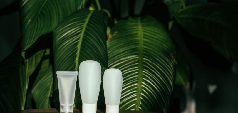 Unbranded white cosmetic tubes in front of large green leaves