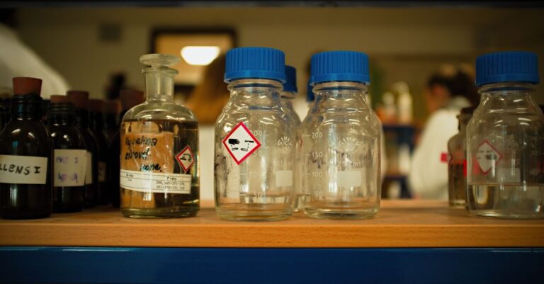 Glass laboratory bottles with hazard labels on a shelf