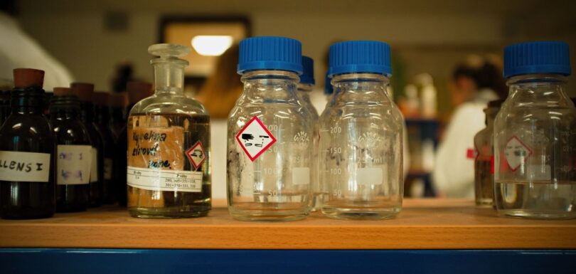 Glass laboratory bottles with hazard labels on a shelf