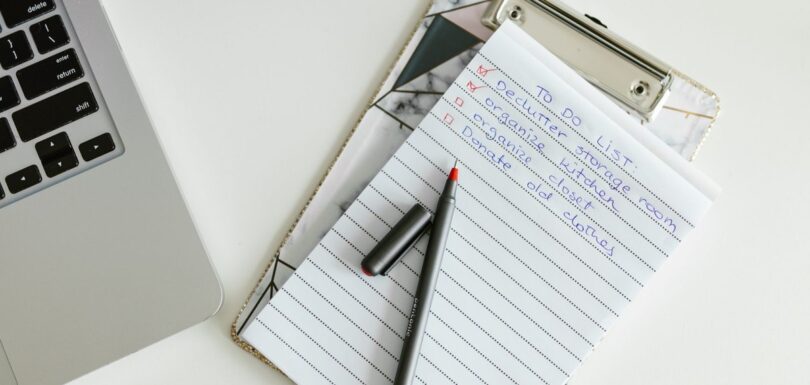 Pen and notepad on a desk beside a laptop and paperwork
