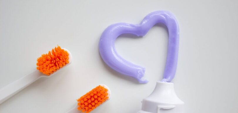 Toothbrushes beside toothpaste squeezed into a heart shape on a white surface