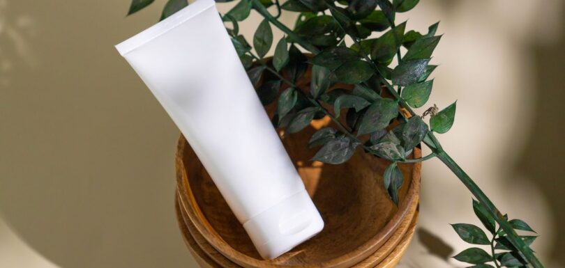 White cosmetic tube beside a green plant